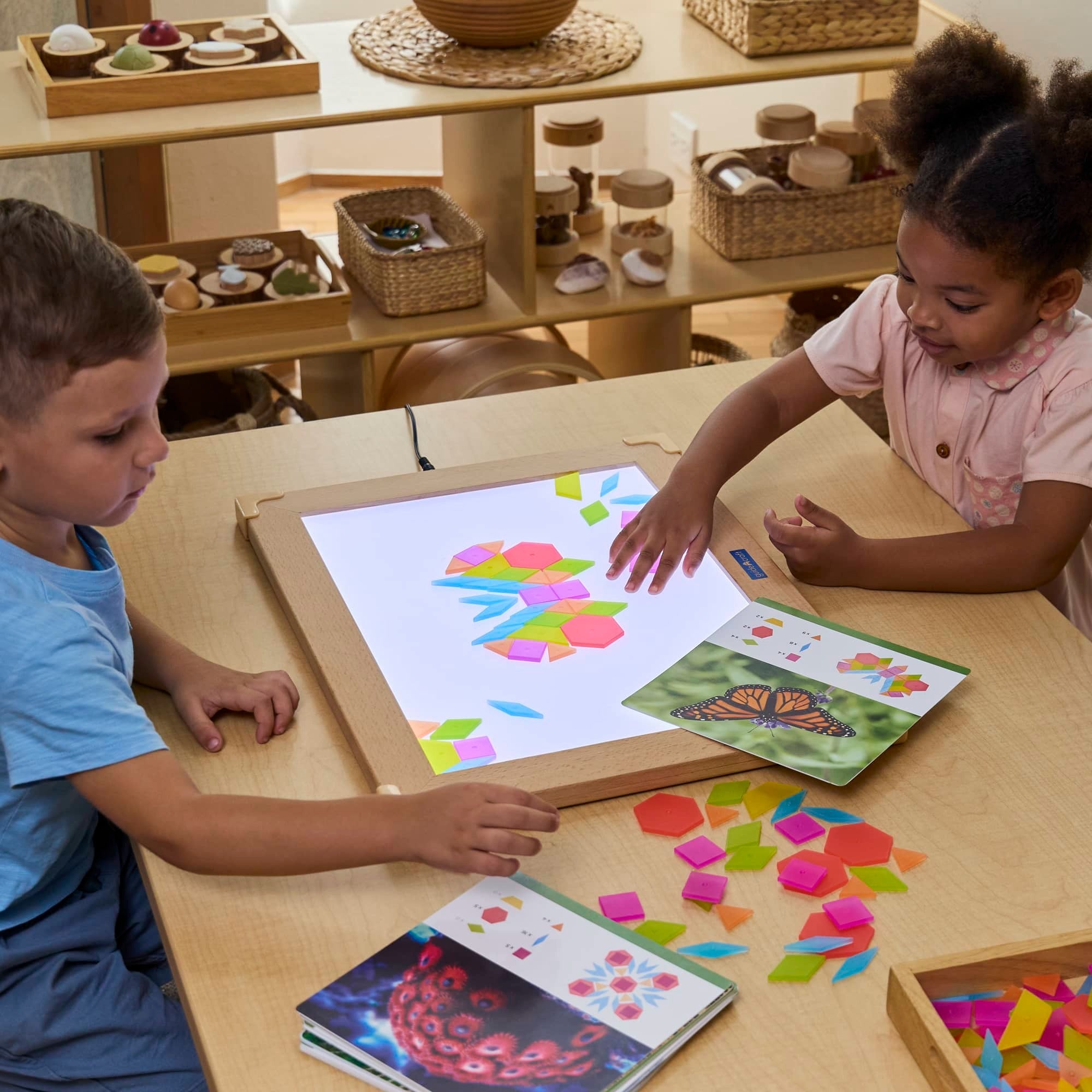 Zwei Kinder spielen mit Guidecraft durchscheinenden Tangram-Fliesen auf einem Leuchttisch, legen geometrische Formen nach Vorlagen für kreatives, lehrreiches Lernen.