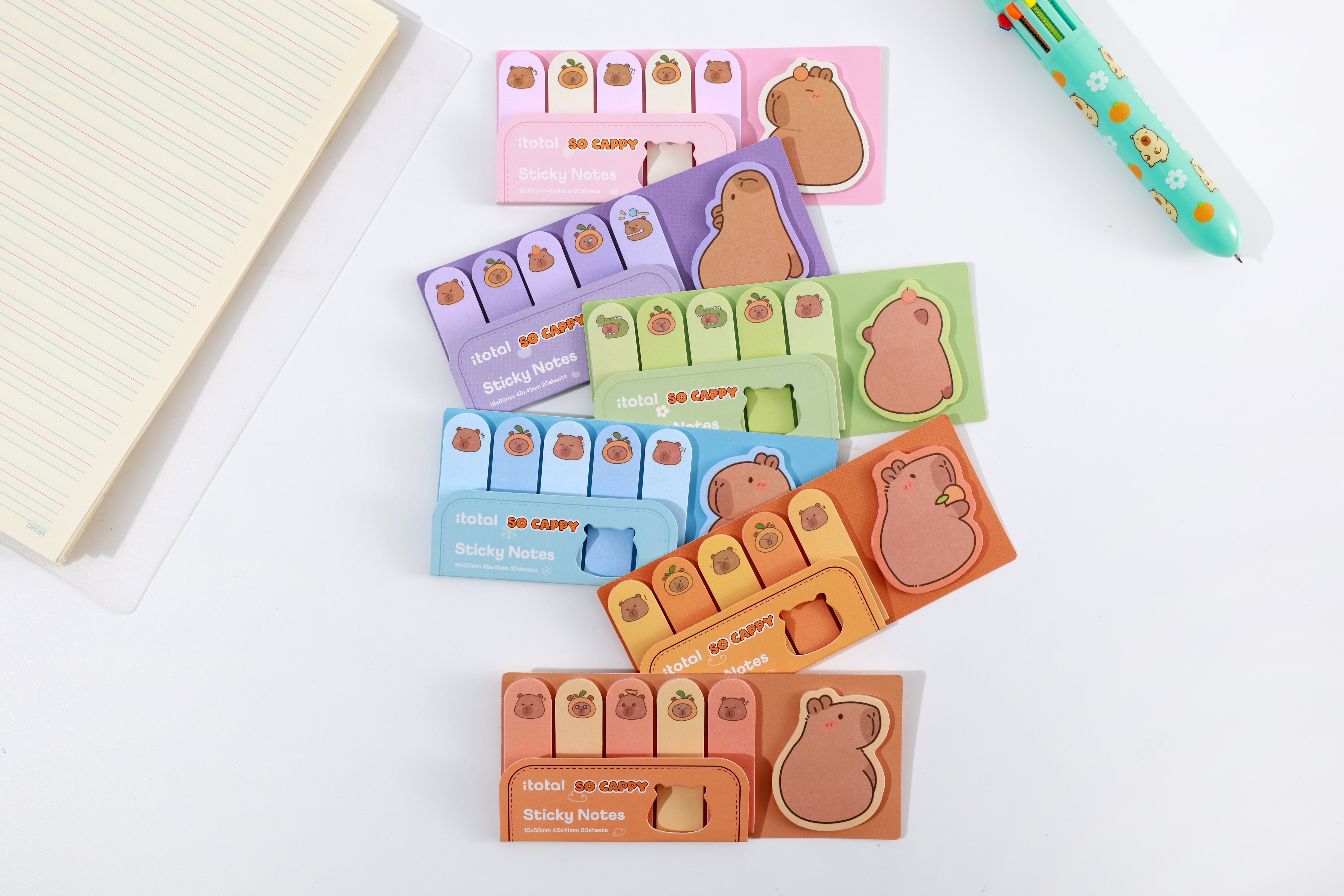 Verschiedene bunte Capybara-Haftnotizen-Sets neben einem passenden Stift auf weißem Grund.
