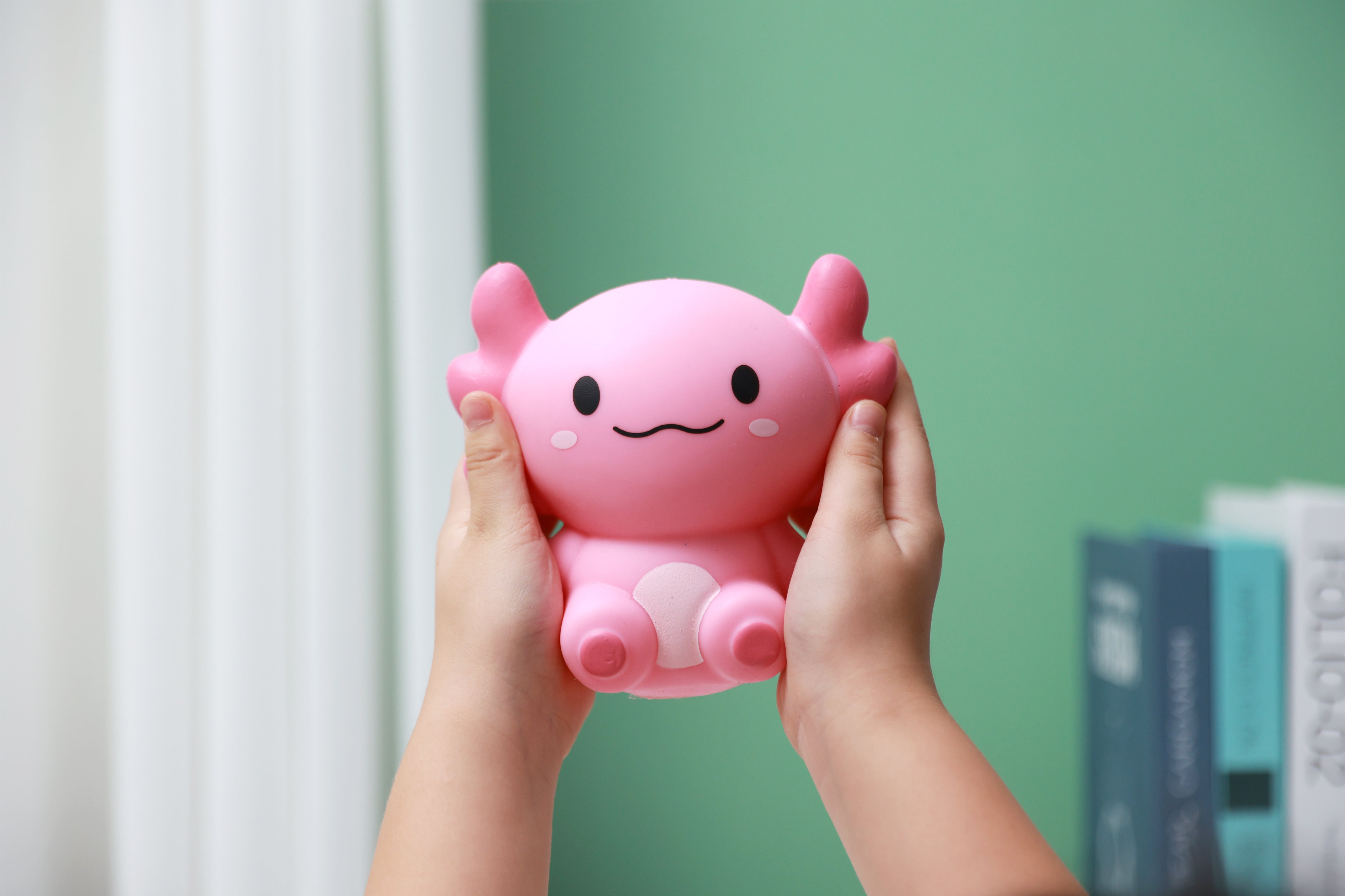 Zwei Hände halten das rosa iTotal Squeeze Axolotl XL, ein weiches Antistress-Spielzeug mit niedlichem Gesichtsausdruck.
