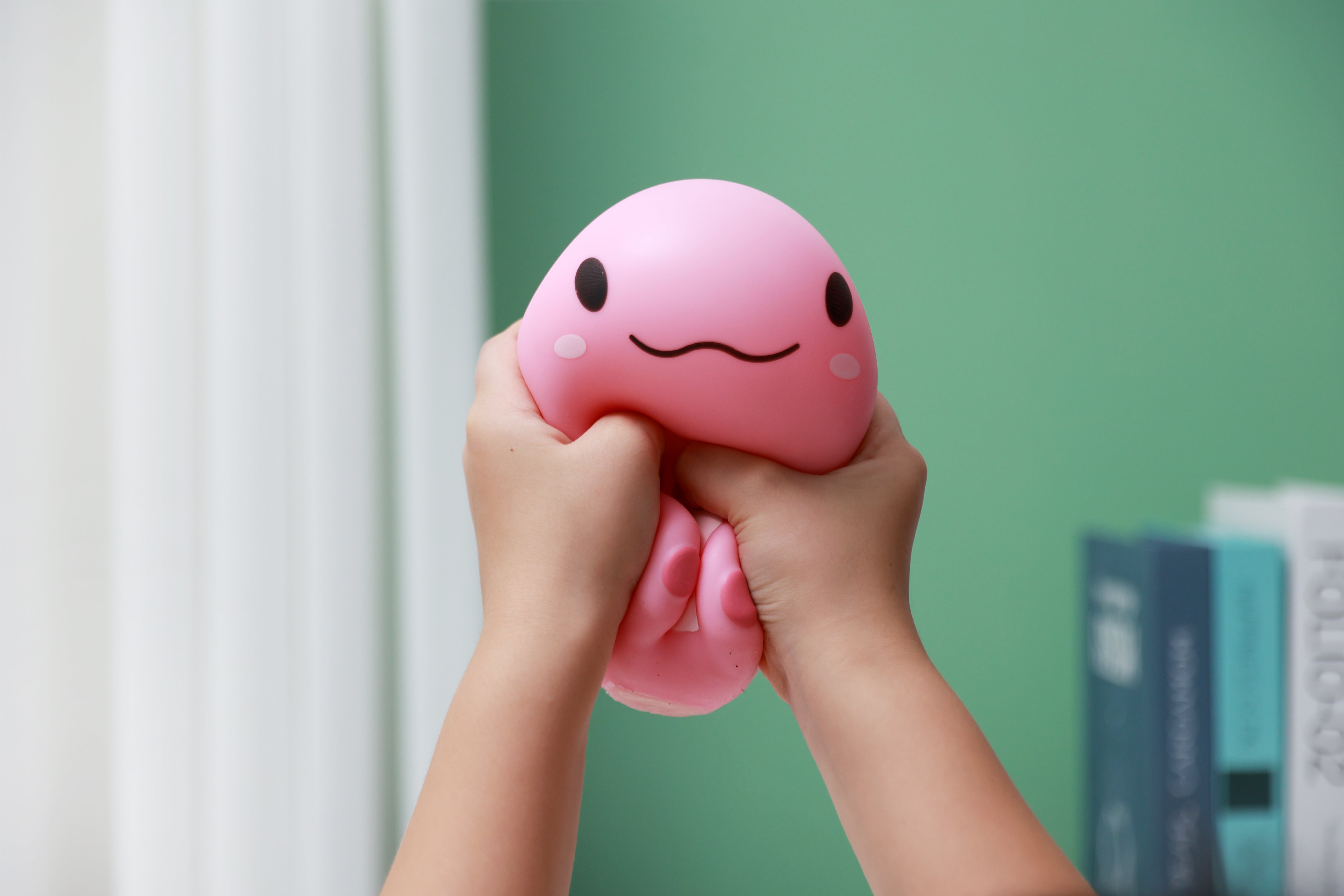 Zwei Hände drücken das rosa iTotal Squeeze Axolotl XL zusammen, um die weiche Antistress-Textur zu zeigen.