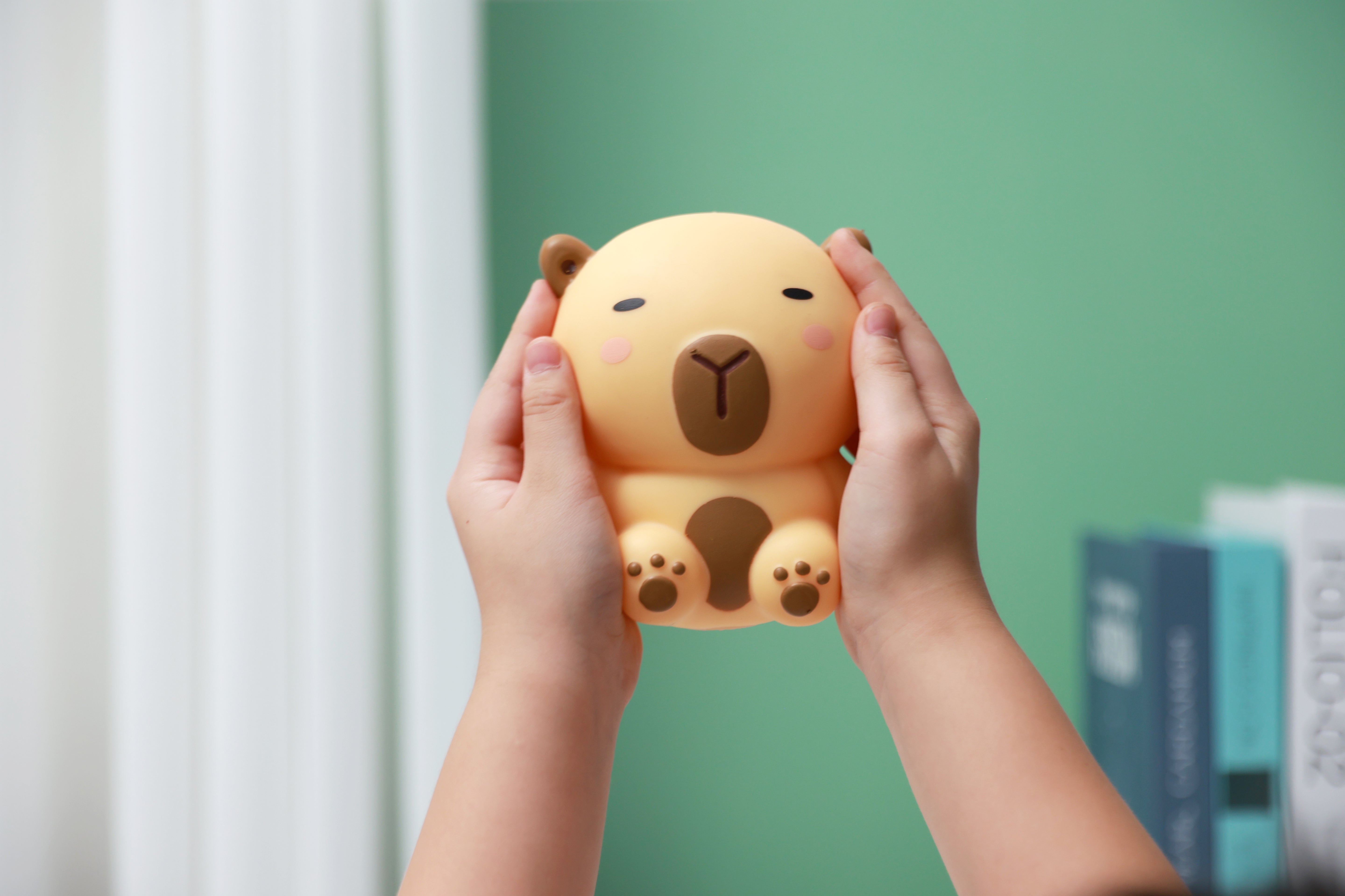 Zwei Hände präsentieren das beigefarbene iTotal Squeeze Capybara XL, ein weiches Antistress-Spielzeug mit entspanntem Gesichtsausdruck.
