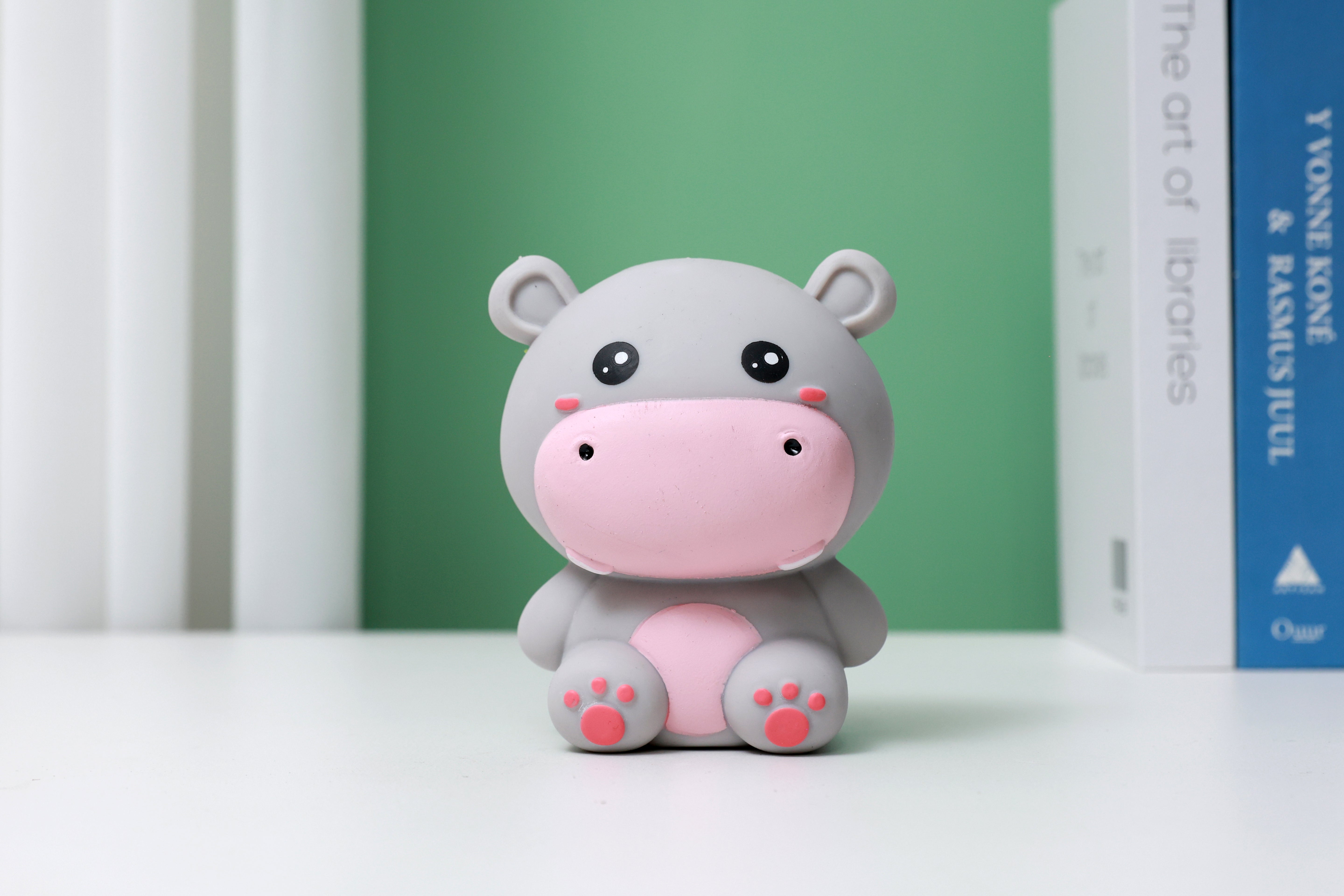 Graues iTotal Squeeze Hippo XL als dekoratives Antistress-Spielzeug auf einem Schreibtisch vor grünem Hintergrund.