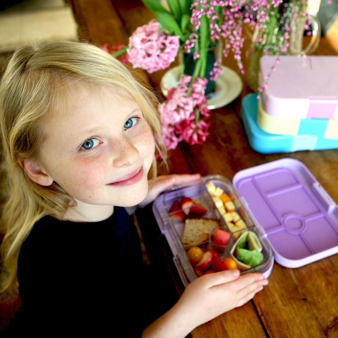 Yumbox Original Lavande Purple, Mädchen mit Lunchbox, Bento Box, lila, geöffnete Brotdose, Obst, Käse, Sandwich, gesundes Pausenbrot, Kinder, Schule, Vesperzeit.