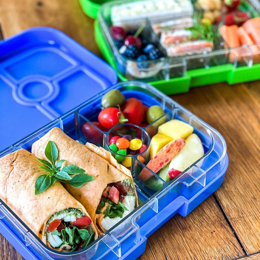 Yumbox Panino Lunchbox, Surf Blue, offen, befüllt mit Wraps, Tomaten, Oliven, Obst, Schokolinsen, Bento-Box, Pausenbrot, Schule, Trennung, gesund, vielseitig.